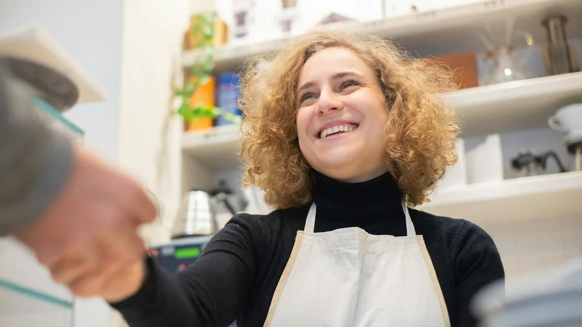 Barista smiling and greeting a customer in a café, showing the moment a positive review is born